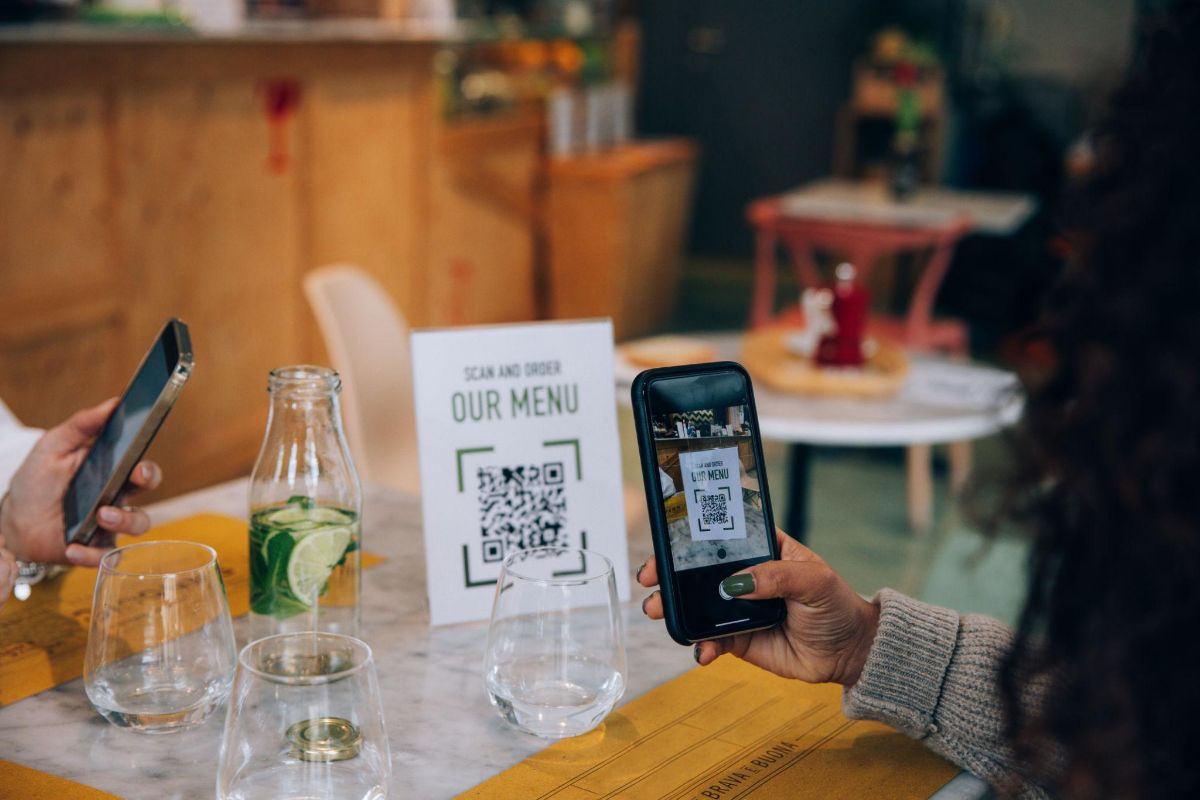 Deux clientes attablées scannent le QR code du menu posé sur la table.