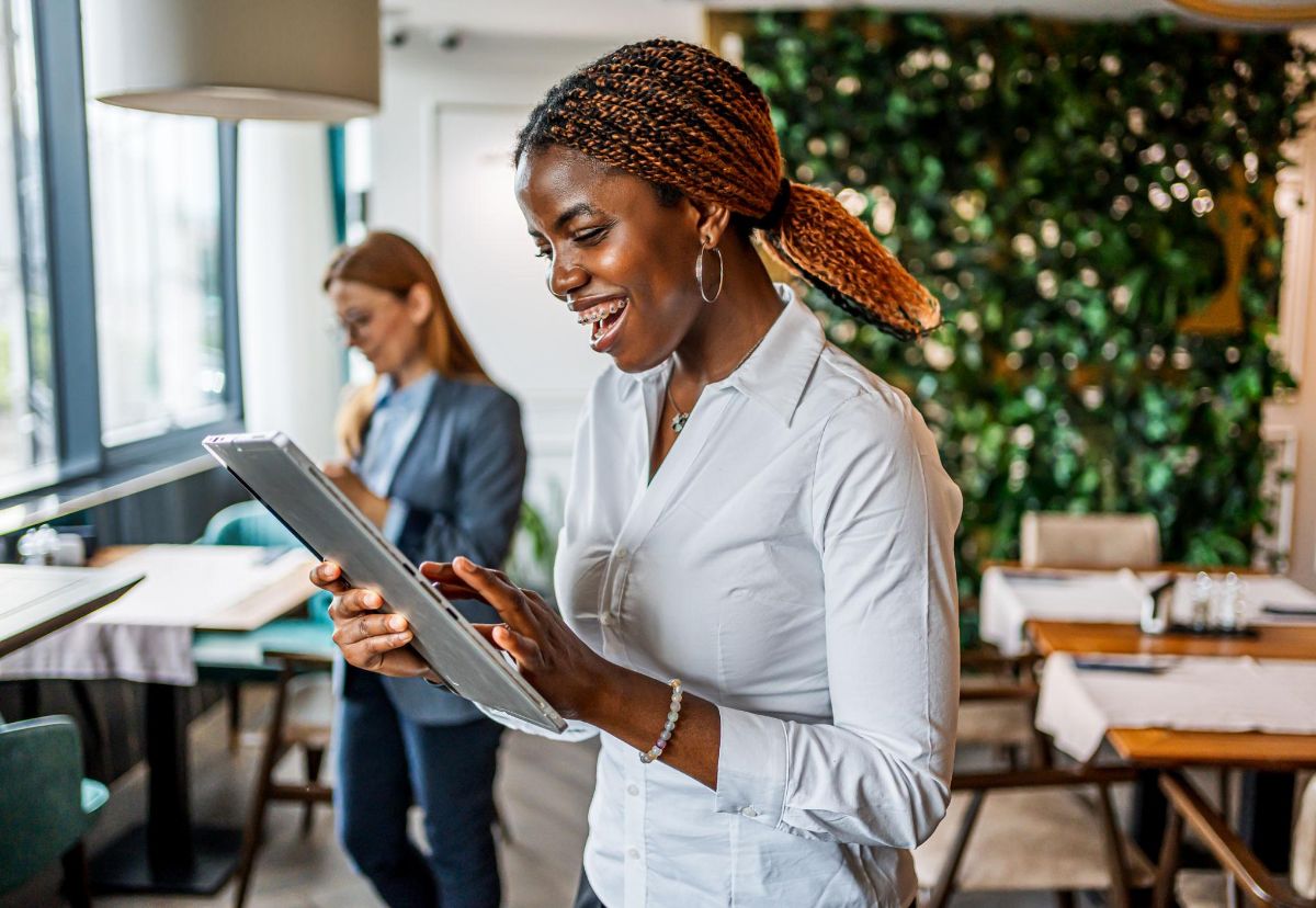 Une responsable de salle consulte une tablette dans la salle de son restaurant.